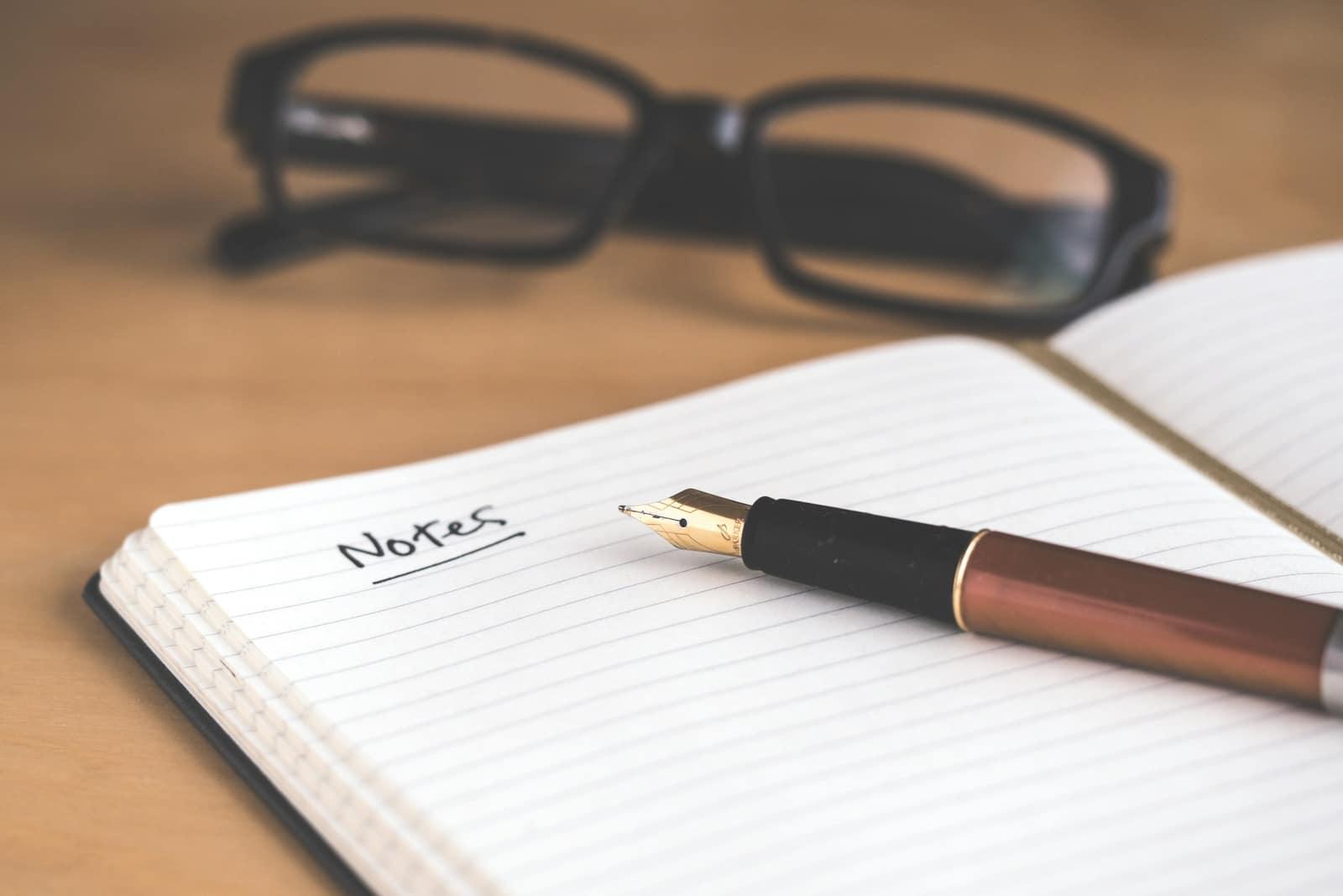 An open notebook headed 'Notes' with a fountain pen and reading glasses