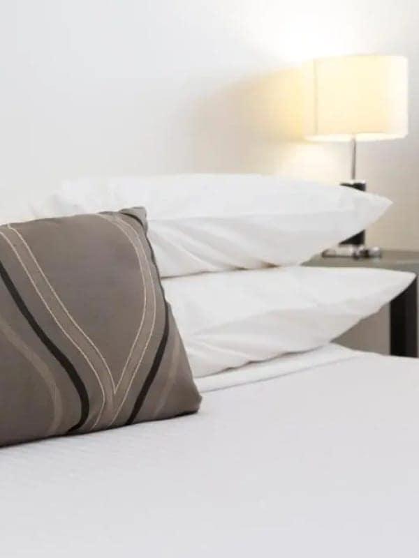 Crisp white pillows and a patterned cushion beside a glowing bedside lamp