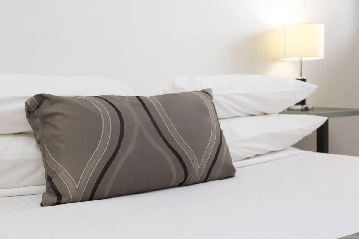 Patterned cushion against crisp white pillows, bedside lamp behind