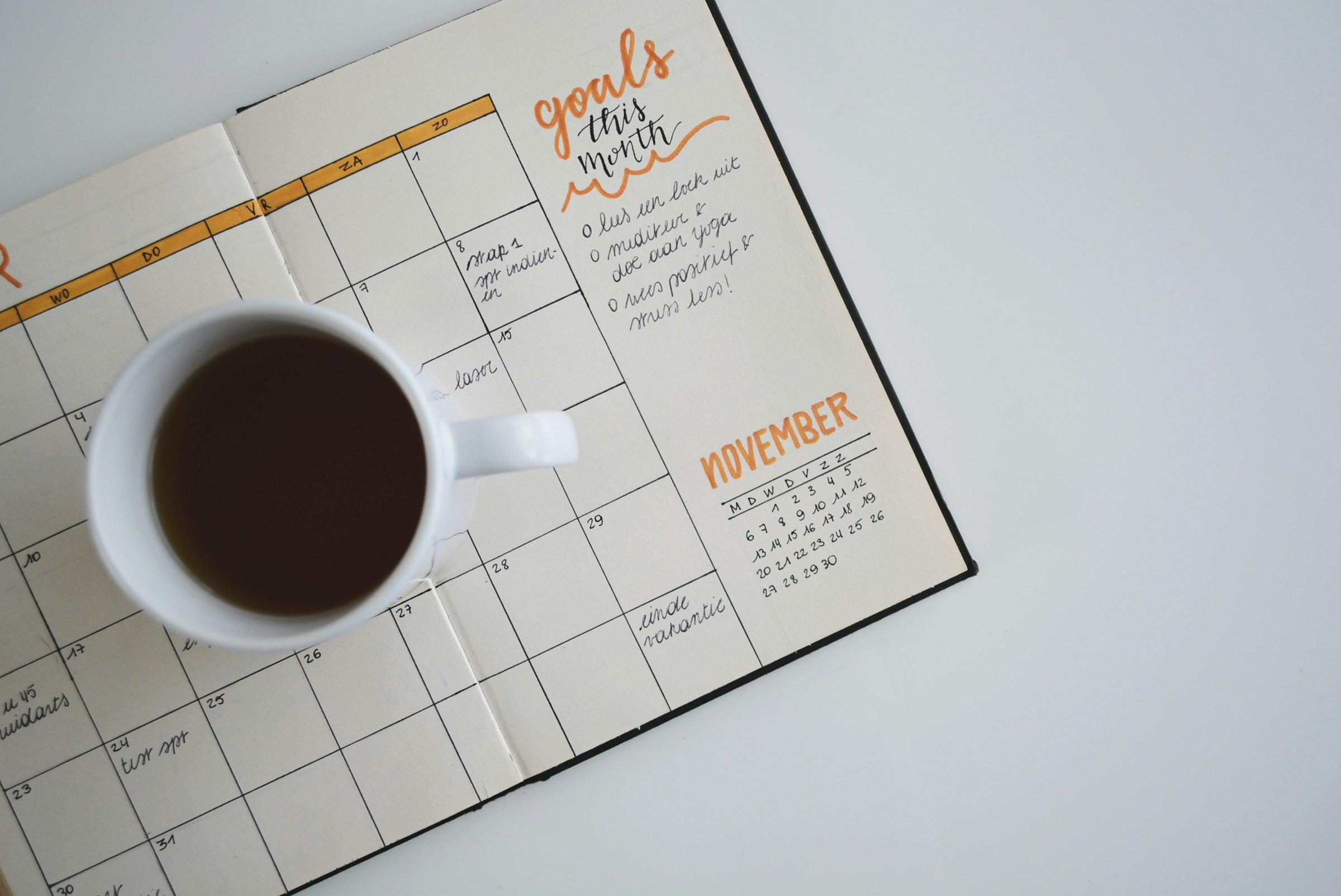 An open monthly planner with handwritten notes and a cup of coffee resting on it