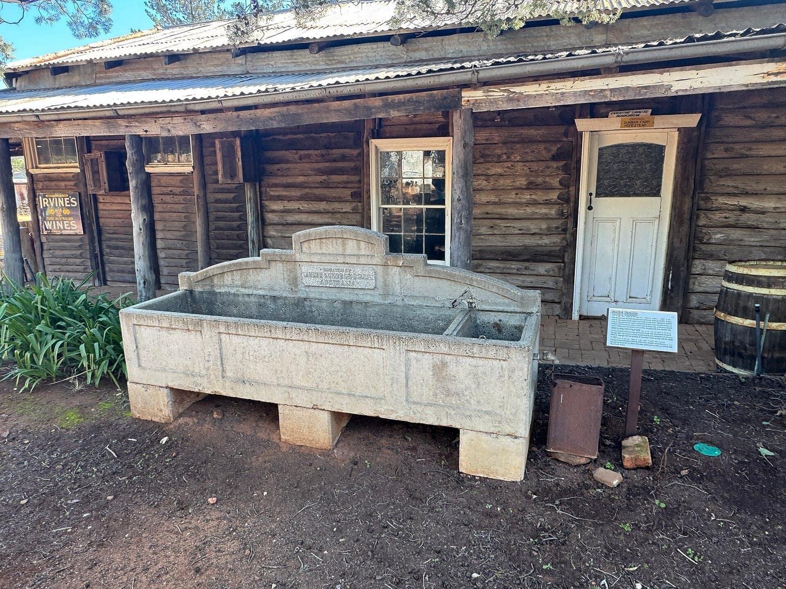A heritage water trough outside a log homestead at Pioneer Park Museum