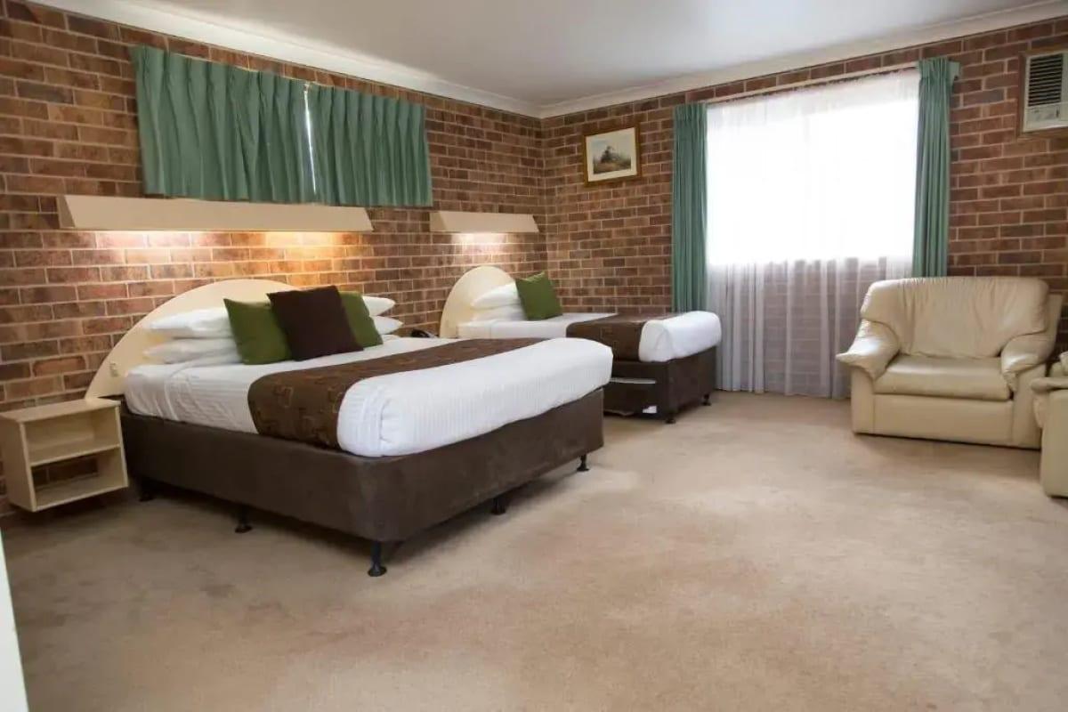 Spacious deluxe room with queen and single beds, green curtains and an armchair by the window