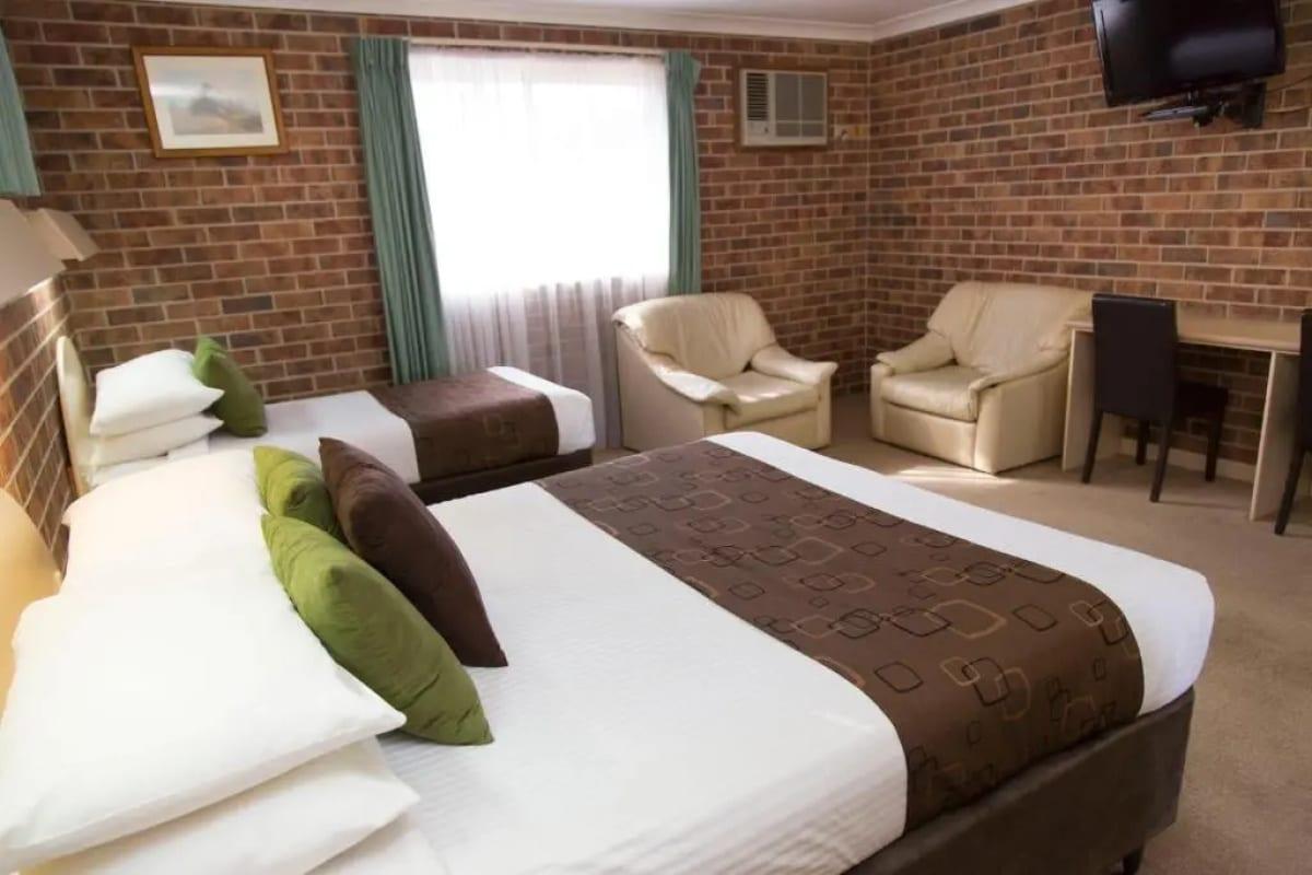 Deluxe queen and single beds with olive cushions, armchairs and a work desk