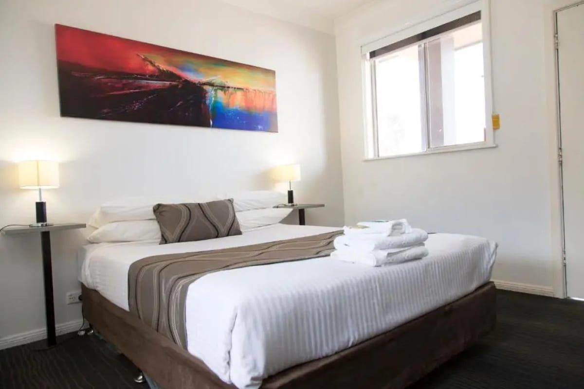 Queen bed with fresh towels laid out, reading lamps either side of a bright window