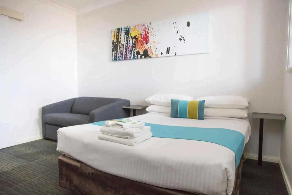 Standard room with teal trim, plump pillows and a lounge chair