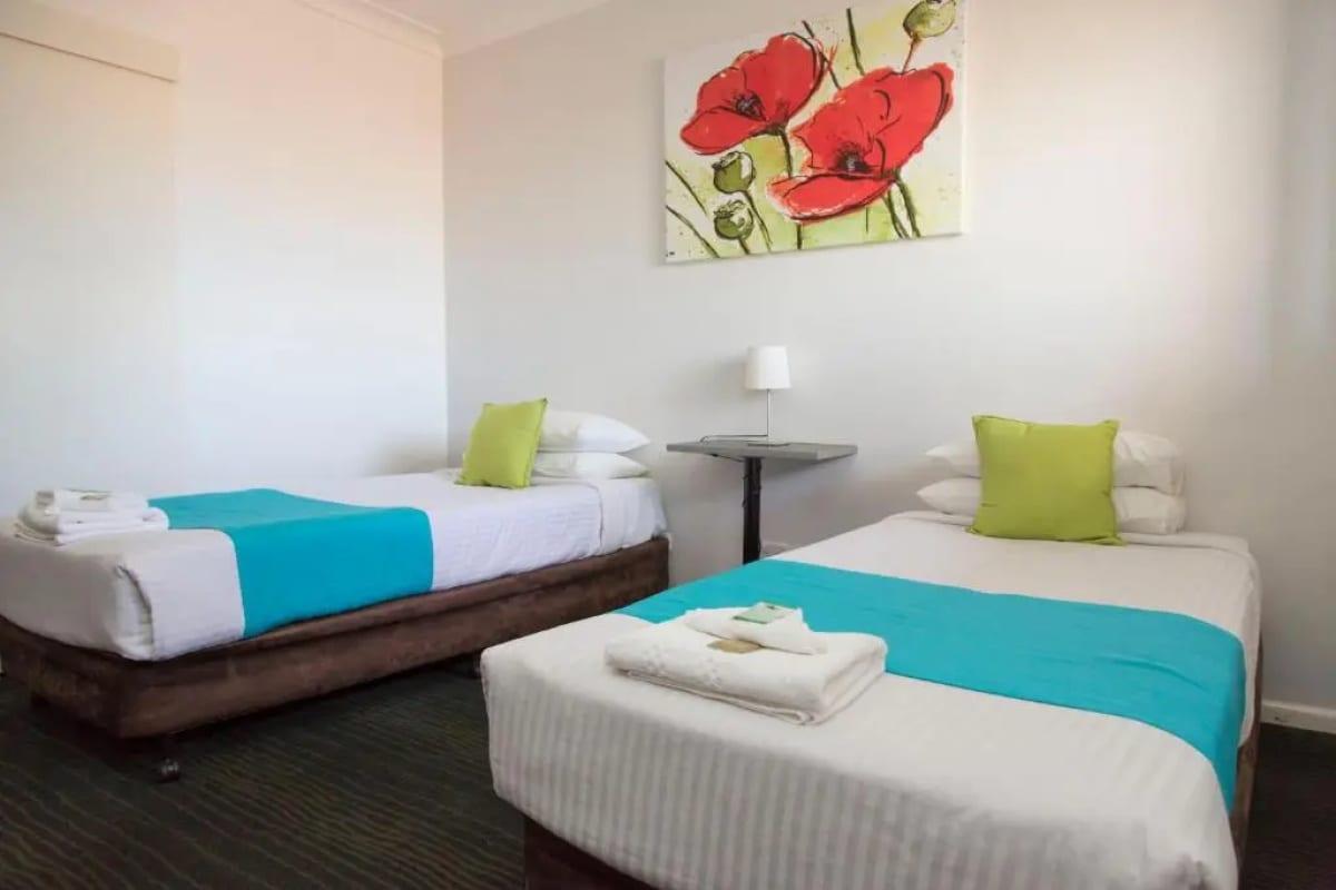 Twin room with two single beds, lime-green cushions and poppy artwork
